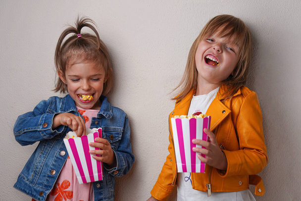 dvě šťastné holčičky jíst sladký popcorn na šedém pozadí - Fotografie, Obrázek