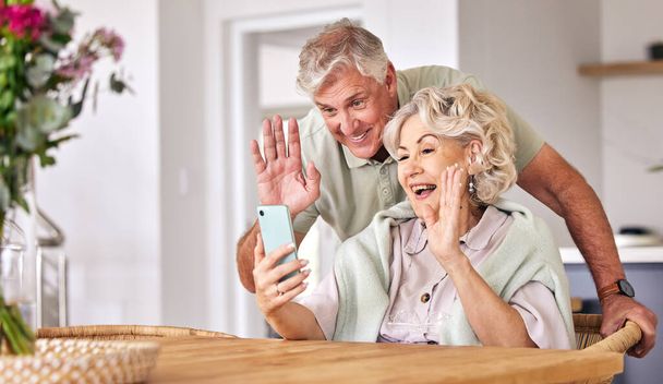 Starší pár, videohovor a vlna s telefonem, konverzací a kontaktem na sociálních sítích v důchodu. Happy starší muž, žena a webinář s smartphonem, úsměv a ahoj v dopoledních hodinách, dům nebo stůl. - Fotografie, Obrázek