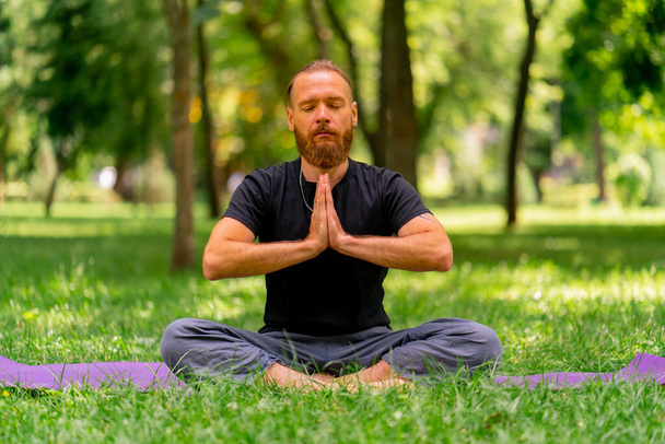 portré jóképű szakállas férfi meditál a parkban ül lótuszpozícióban gyakorló jóga zen egészséges életmód nyugodt meditáció - Fotó, kép