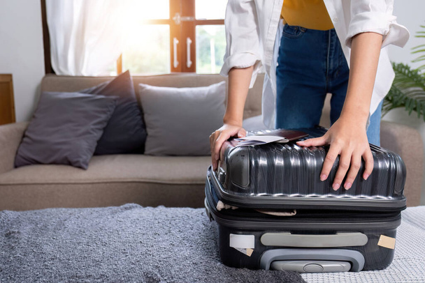 Frau versucht einen Koffer voller Habseligkeiten zu schließen, um sich auf Urlaubsreise vorzubereiten.. - Foto, Bild
