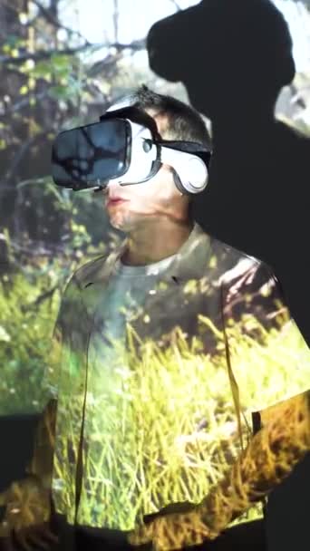 Fiatal férfi alkalmi ruhák és VR szemüveg fű kép áll a fény vetítés és mozgó karok mosollyal - Felvétel, videó