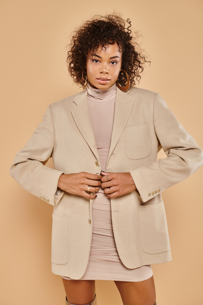 autumn fashion, stylish african american woman posing in tight dress and blazer on beige backdrop - Foto, afbeelding