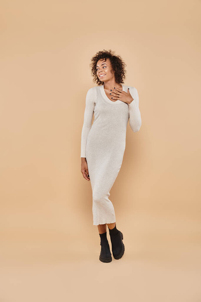 curly african american woman posing in midi dress and boots on beige backdrop, autumn fashion - Photo, Image