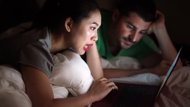 Aziatisch vrouw liggend op een bed in de buurt inhoud vriendje in casual dragen terwijl het kijken naar een film op een laptop thuis. - Video