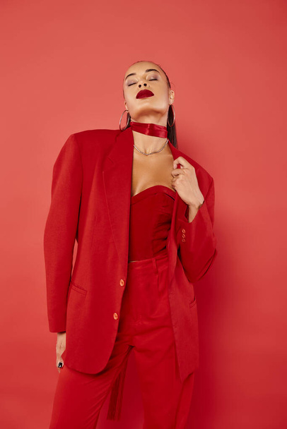 beautiful african american woman with ponytail posing with closed eyes in suit on red background - Foto, Imagem