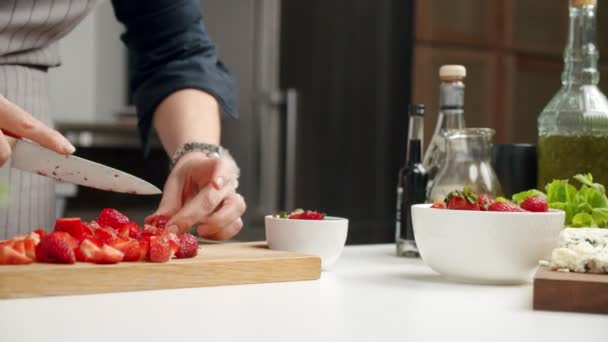 Gezichtsloze anonieme persoon snijden verse rijpe aardbeien op houten plank tijdens het koken risotto in de keuken - Video