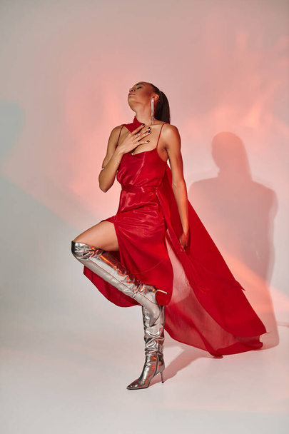 młoda Afroamerykanka w czerwonej sukience z szalikiem w srebrnych butach na szarości z oświetleniem - Zdjęcie, obraz