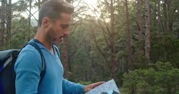 Homem com mochila e bengala examinando mapa de papel enquanto caminhava na floresta no fim de semana - Filmagem, Vídeo