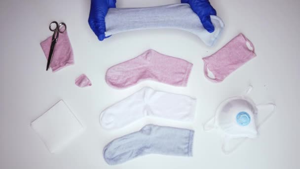 Fentről arctalan személy kék steril kesztyűben fehér szalvétát tesz a pamut zokniba, miközben arcmaszkot készít otthon a COVID 19 alatt. - Felvétel, videó
