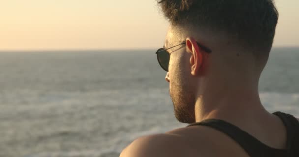Vue arrière de l'athlète masculin musclé en tenue de sport debout sur la plage et profitant du coucher du soleil après l'entraînement en été - Séquence, vidéo