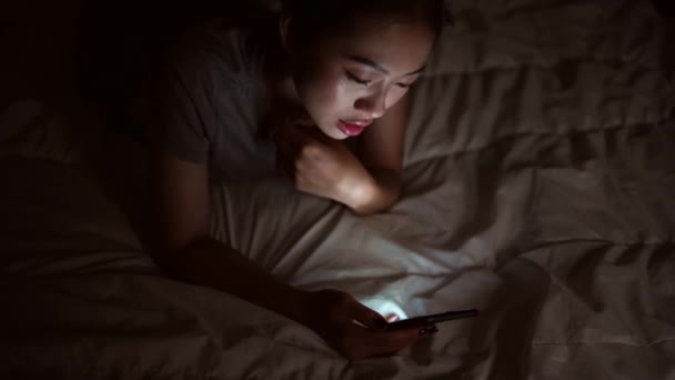 Ασιάτισσα ξαπλωμένη σε κρεβάτι χρησιμοποιώντας smartphone στο σπίτι. - Πλάνα, βίντεο