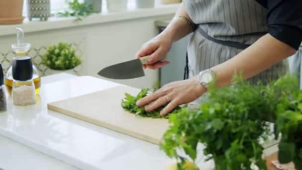 Real time hoge hoek van gewas anonieme vrouw met mes hakken groene peterselie bladeren op houten snijplank tijdens het koken in de keuken - Video
