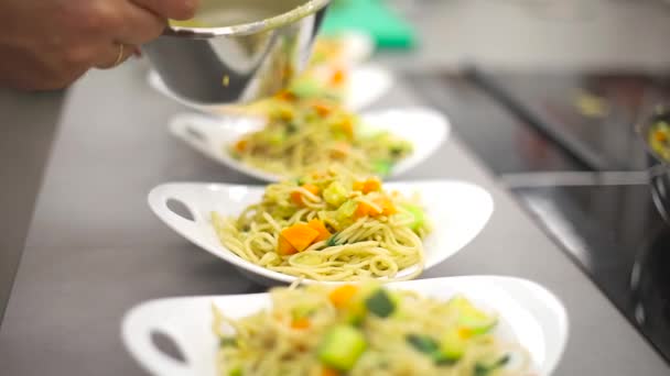 Crop man valkoinen kokki takki kaatamalla kastike lautaselle pastaa ruostumattomasta pannusta seisoessaan ravintolan keittiössä - Materiaali, video