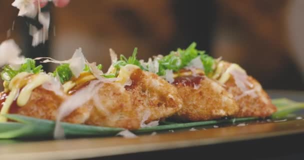 Unbekannter Koch verschüttet dünne Bonito-Flocken auf traditionellen japanischen gebratenen Klößen, die Gyozas genannt werden und sich auf Plattform im Restaurant drehen - Filmmaterial, Video