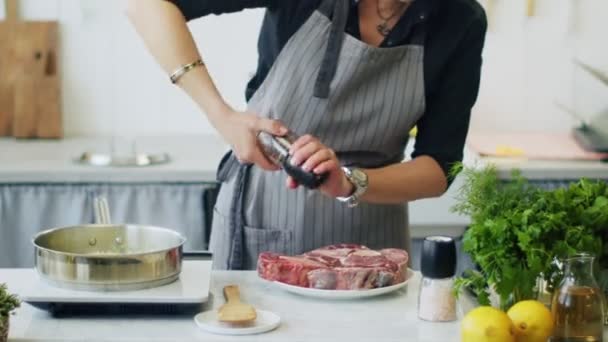 Real time of crop unrecognizable female in apron adding pepper from mill on raw veal shank while preparing ossobuco - Footage, Video