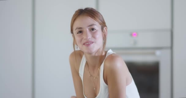 Selbstbewusste junge Millennials mit langen Ingwerhaaren in weißem Top, strahlend berührtem Gesicht und Blick in die Kamera in der modernen Küche zu Hause - Filmmaterial, Video