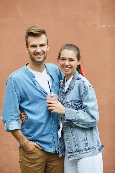 Portrait of happy modern young couple in casual clothing cuddling each other against building wall - Foto, immagini