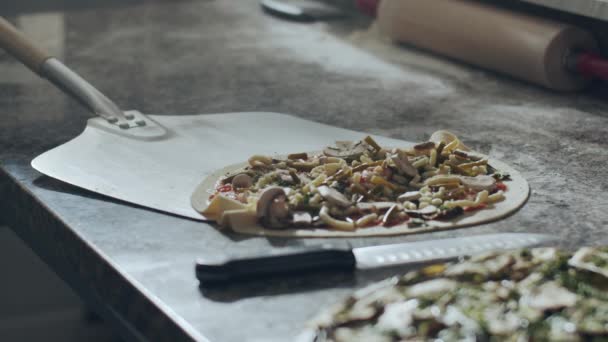 Oříznutý anonymní kuchař s kovovou lopatou s tradiční italskou syrovou pizzou připravenou na pečení z mramorového stolku do trouby na pečení v kuchyni restaurace - Záběry, video