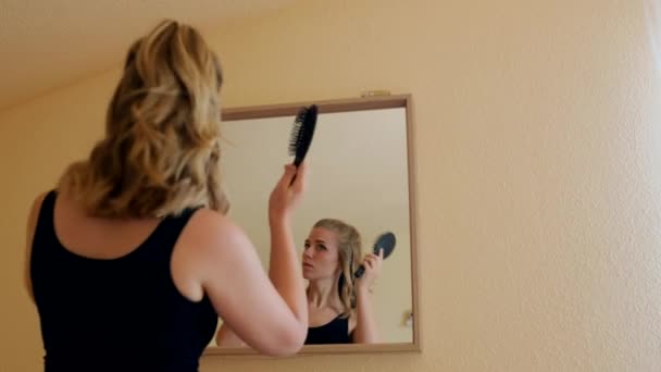 Matala kulma takaisin näkymä nuori nainen rento asu harjaus hiukset ja tehdä poninhäntä seisoessaan peilin edessä kotona - Materiaali, video