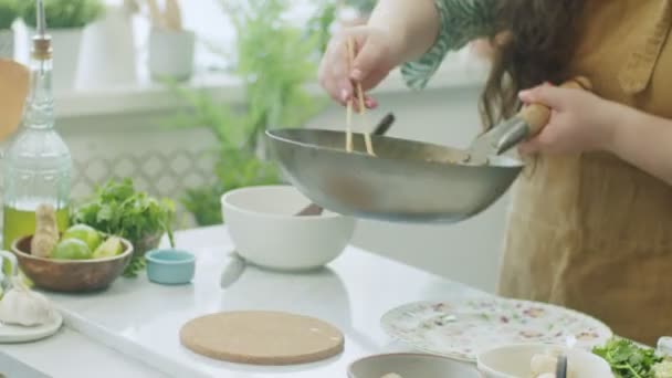 Tempo reale di raccolto anonimo femminile con bacchette in grembiule che serve deliziosi tagliatelle tradizionali asiatiche wok su piatto di ceramica a tavola con piatti in cucina - Filmati, video