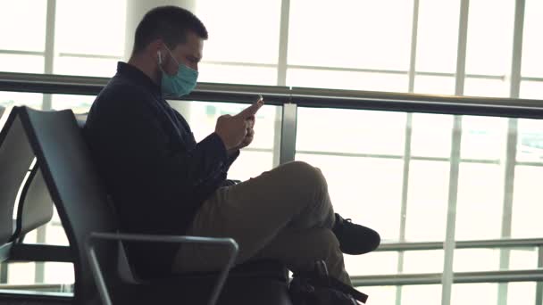 чоловічий турист в медичній масці з використанням мобільного телефону під час очікування польоту в аеропорту - Кадри, відео