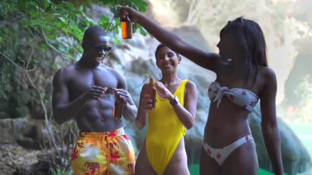Boldog változatos férfi és nő egy üveg sörrel énekel és táncol, miközben a napsütéses nyári napot a tiszta tó partján tölti - Felvétel, videó