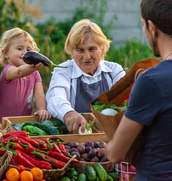 Grootmoeder en kleindochter verkopen groenten en fruit op de boerenmarkt. Selectieve focus. levensmiddelen. - Foto, afbeelding