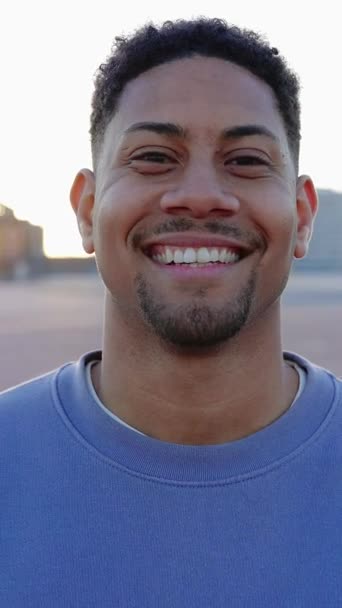 若いヒスパニック系ラテン系男性が屋外で微笑んでいる. ハッピークローズアップ 市街地のカメラでポーズミレニアル10代の男の子の顔の肖像画. 縦9:16スクリーン映像. - 映像、動画