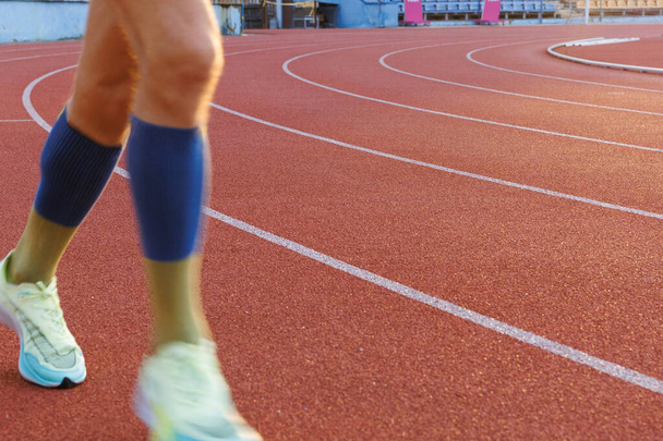 Juoksijan puoliksi sumentuneet jalat liikkuvat juoksuradalla stadionin ympärillä. Objekti vasemmalla, tilaa tekstille. - Valokuva, kuva