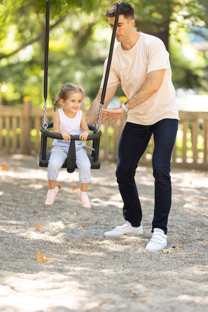 Muž jezdící na své dceři na houpačkách v letním parku. Střední snímek - Fotografie, Obrázek