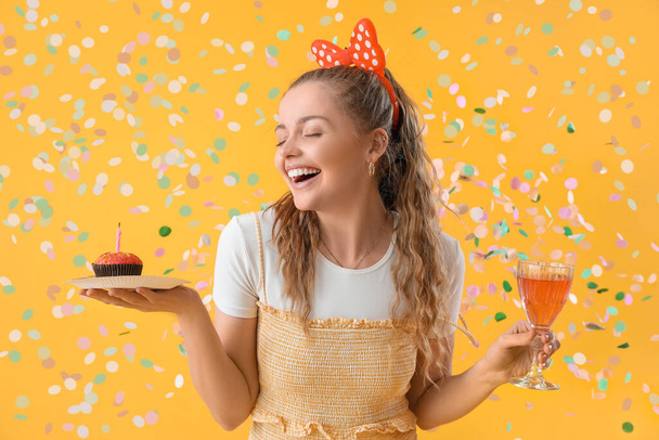 Happy young woman with Birthday muffin and drink on yellow background - Photo, Image