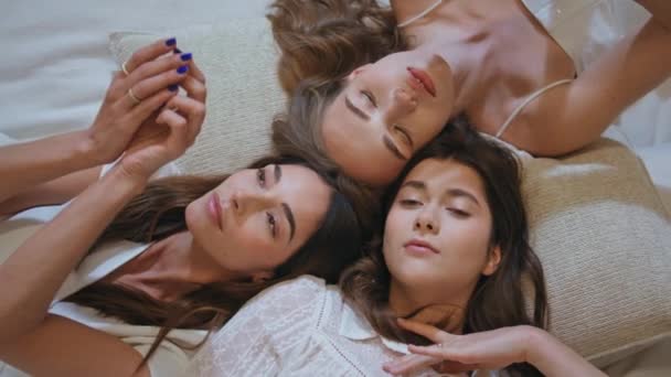 Beautiful women lying together closeup. Top view peaceful girls gently touching dancing with hands. Attractive dreamy models looking camera resting at cozy place. Natural beauty femininity concept. - Footage, Video