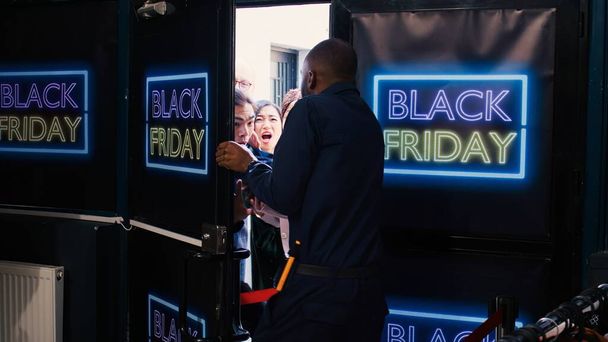 Een menigte van diverse klanten bij de ingang duwen om de voordeur te openen, gek worden op zwarte vrijdag. Mensen die ruzie maken met een Afro-Amerikaanse veiligheidsagent die in de rij staat. Koopjesjacht. - Foto, afbeelding