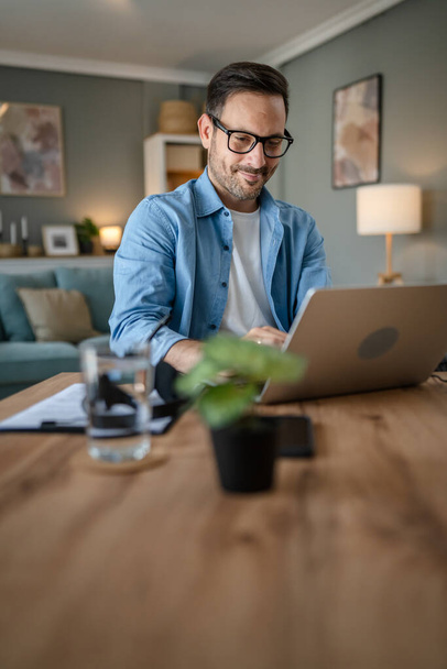 een man volwassen blanke man met baard werk op zijn laptop computer thuis gelukkig glimlach succes freelance ondernemer of remote werk concept - Foto, afbeelding