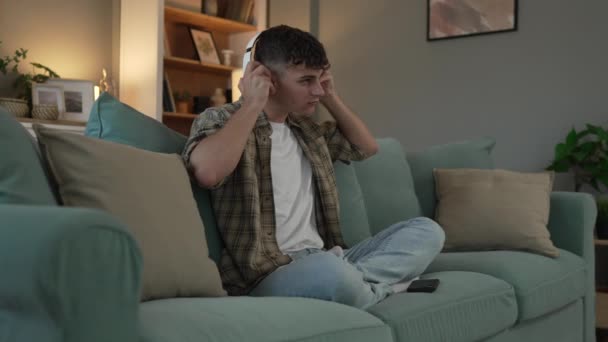Ένας έφηβος άνδρας νεαρός καυκάσιος άντρας χρησιμοποιεί ακουστικά για online καθοδηγούμενη πρακτική διαλογισμού mindfulness yoga με τα μάτια κλειστά στο σπίτι πραγματικοί άνθρωποι αυτο-φροντίδα εκδήλωση έννοια αργή κίνηση γενιάς Z - Πλάνα, βίντεο