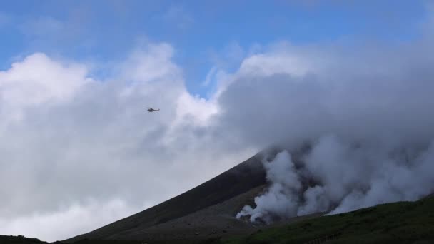 Аварийный вертолет-медиум пролетает над паровыми вентиляционными отверстиями на горе. Асахи на Хоккайдо, Япония. Высококачественные 4k кадры - Кадры, видео