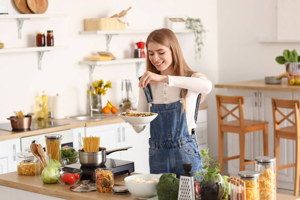 Young woman spicing tasty pasta in kitchen - Photo, Image
