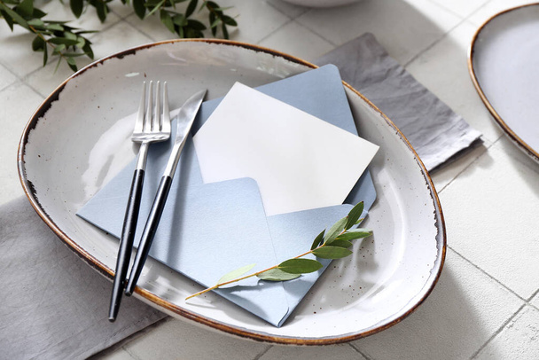 スタイリッシュなテーブル設定、白いタイルの背景に空白のカードと植物の枝を持つ封筒 - 写真・画像