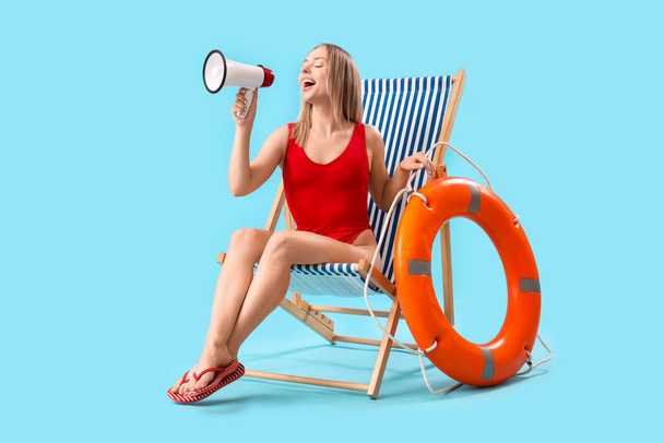 Beautiful woman with megaphone, deck chair and ring buoy on blue background - Photo, Image