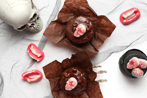 Komposition mit leckeren Schokoladenkuchen mit Bonbons und Totenkopf für die Halloween-Feier auf weißem Hintergrund, Nahaufnahme - Foto, Bild