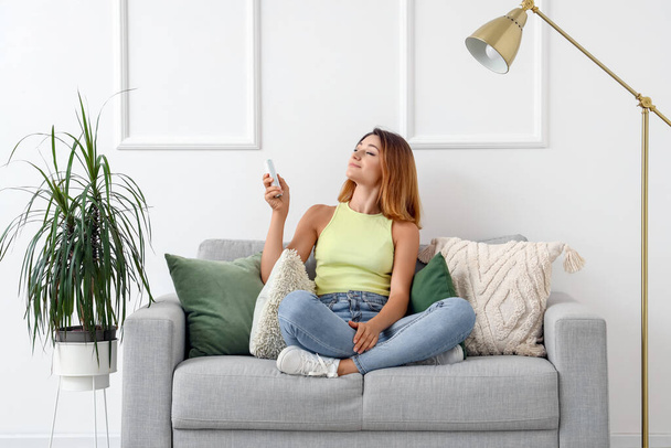 Nuori nainen kytkemällä ilmastointilaite kotona
 - Valokuva, kuva