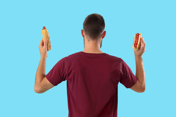 Junger Mann mit leckeren Hot Dogs auf blauem Hintergrund, Rückseite - Foto, Bild
