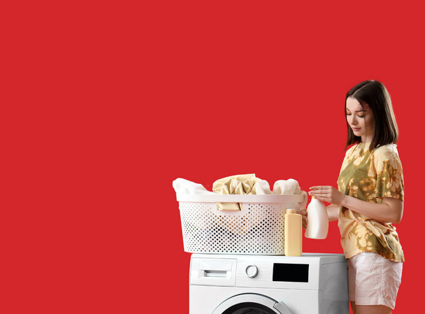Giovane donna con detersivo per bucato e lavatrice su fondo rosso - Foto, immagini