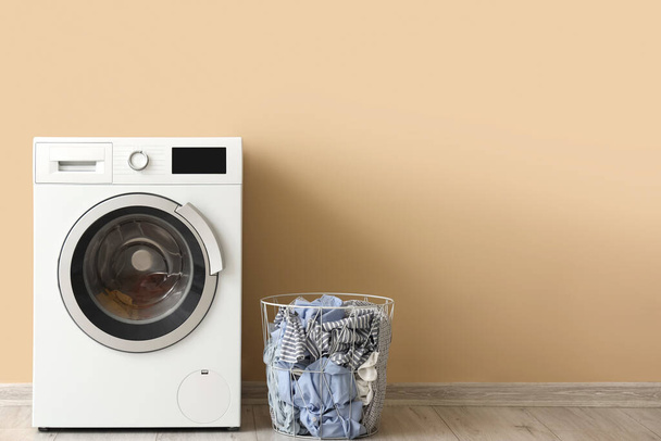Сучасна пральна машина з кошиком для білизни біля бежевої стіни - Фото, зображення