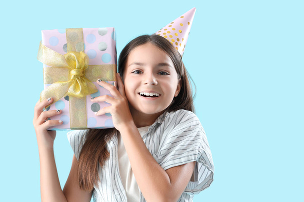 Glückliches kleines Mädchen mit Geburtstagsgeschenkbox auf blauem Hintergrund - Foto, Bild