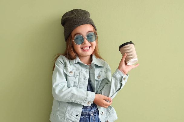 Cute little girl in sunglasses with cup on green background - Photo, Image