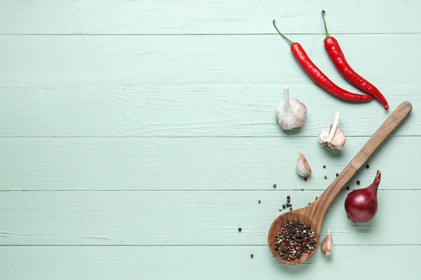 Dřevěná lžička s chilli papričkami, kořením a česnekem na zeleném dřevěném kuchyňském stole - Fotografie, Obrázek