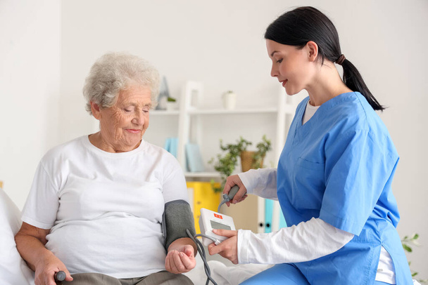 女性看護師が寝室で高齢女性の血圧を測定 - 写真・画像