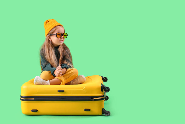 Cute little girl sitting on suitcase against green background - Foto, immagini