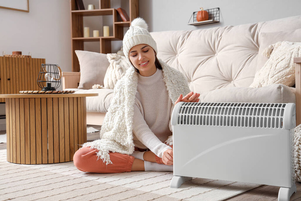 Mujer joven con las manos de calentamiento a cuadros cerca del radiador en casa - Foto, imagen